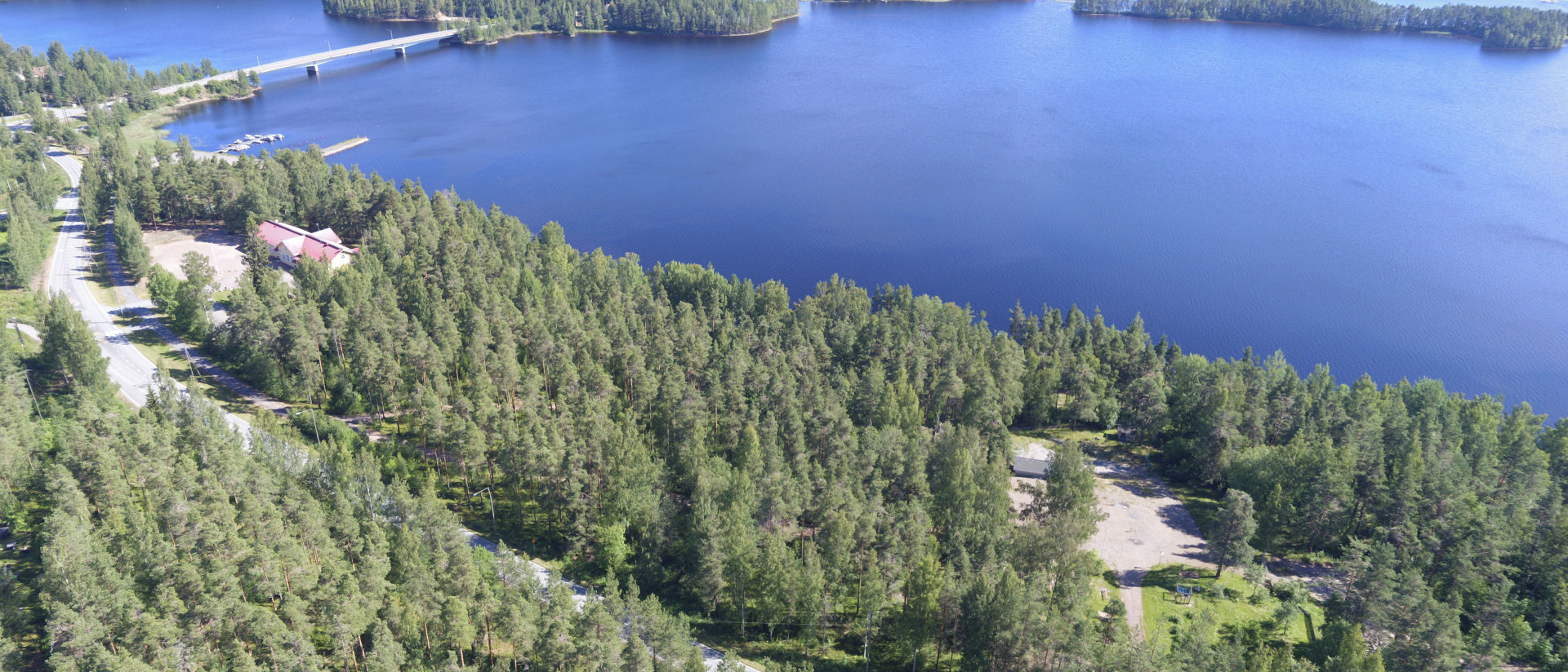 Ilmakuva Vaittilanrannasta Ukonsalmea kohti, etualalla metsää ja autotie, taka-alalla järvi